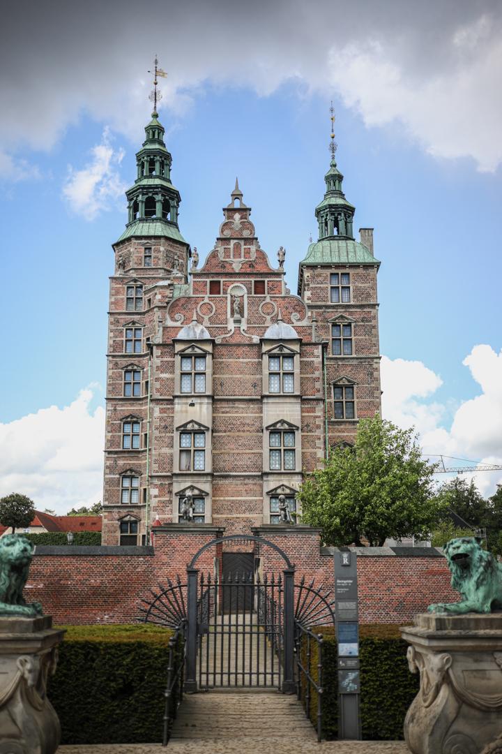 Vue frontale du château de Rosenborg à Copenhague, un imposant bâtiment en briques rouges avec ses deux tours et ses toits en cuivre.